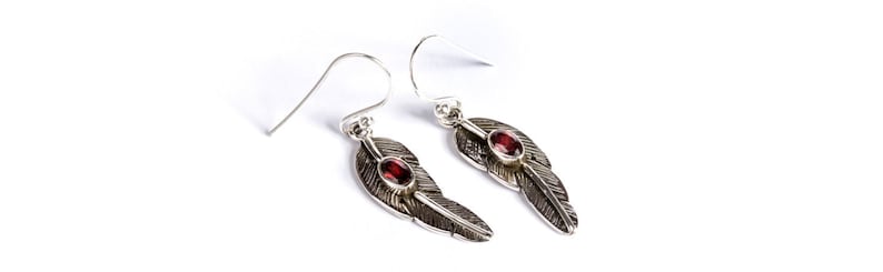 May include: Silver dangle earrings with a feather design and a red gemstone accent.
