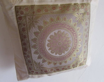 May include: A cream-colored pillow with a gold and pink embroidered design. The design features a large floral motif in the center surrounded by smaller floral patterns.