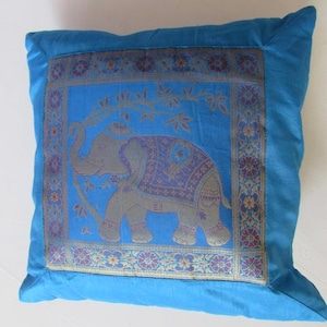 May include: A blue throw pillow with a gold and purple embroidered elephant design. The elephant is standing on a branch with leaves. The pillow has a decorative border.