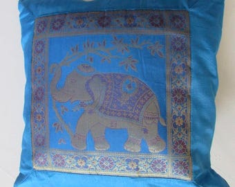 May include: A blue throw pillow with a gold and purple embroidered elephant design. The elephant is standing on a branch with leaves. The pillow has a decorative border.