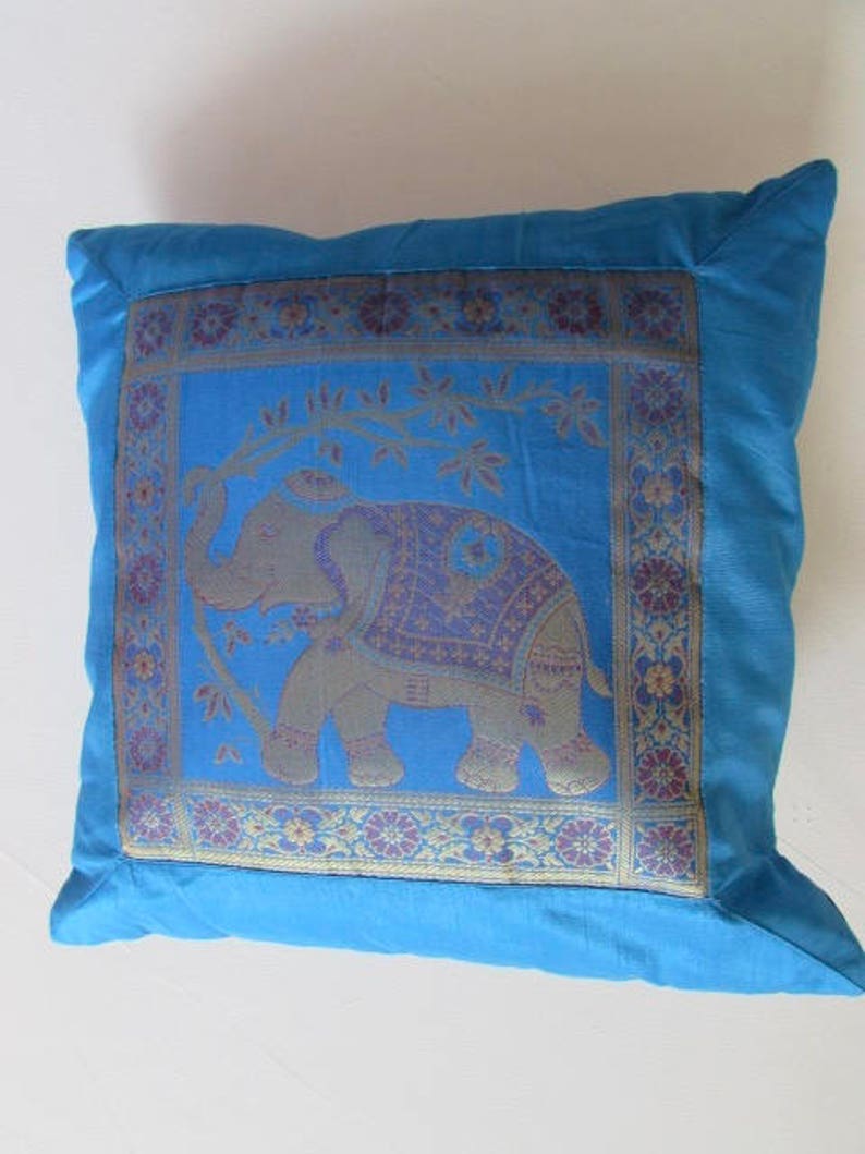 May include: A blue throw pillow with a gold and purple embroidered elephant design. The elephant is standing on a branch with leaves. The pillow has a decorative border.