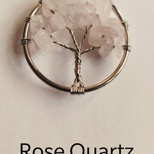 Puede incluir: Un colgante de &aacute;rbol de la vida envuelto en alambre plateado con piedras de cuarzo rosa.