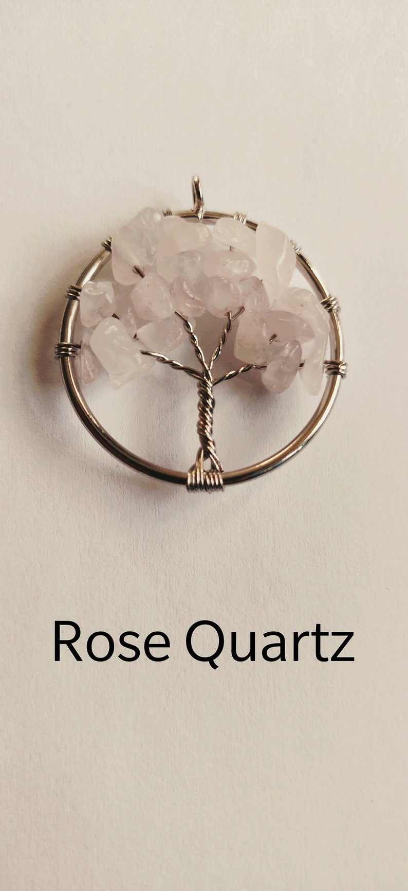 Puede incluir: Un colgante de &aacute;rbol de la vida envuelto en alambre plateado con piedras de cuarzo rosa.