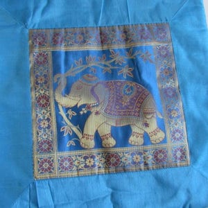 May include: A blue throw pillow with a square embroidered panel featuring a gold and purple elephant on a blue background. The panel is surrounded by a gold and burgundy border with floral designs.