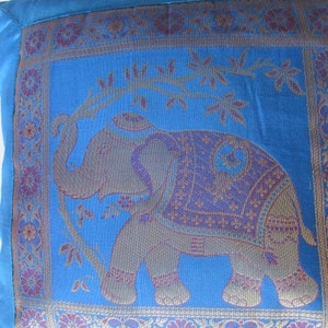 May include: Blue throw pillow with an embroidered elephant design. The elephant is standing on a vine with leaves and flowers. The pillow has a decorative border with floral patterns in shades of purple, gold, and blue.