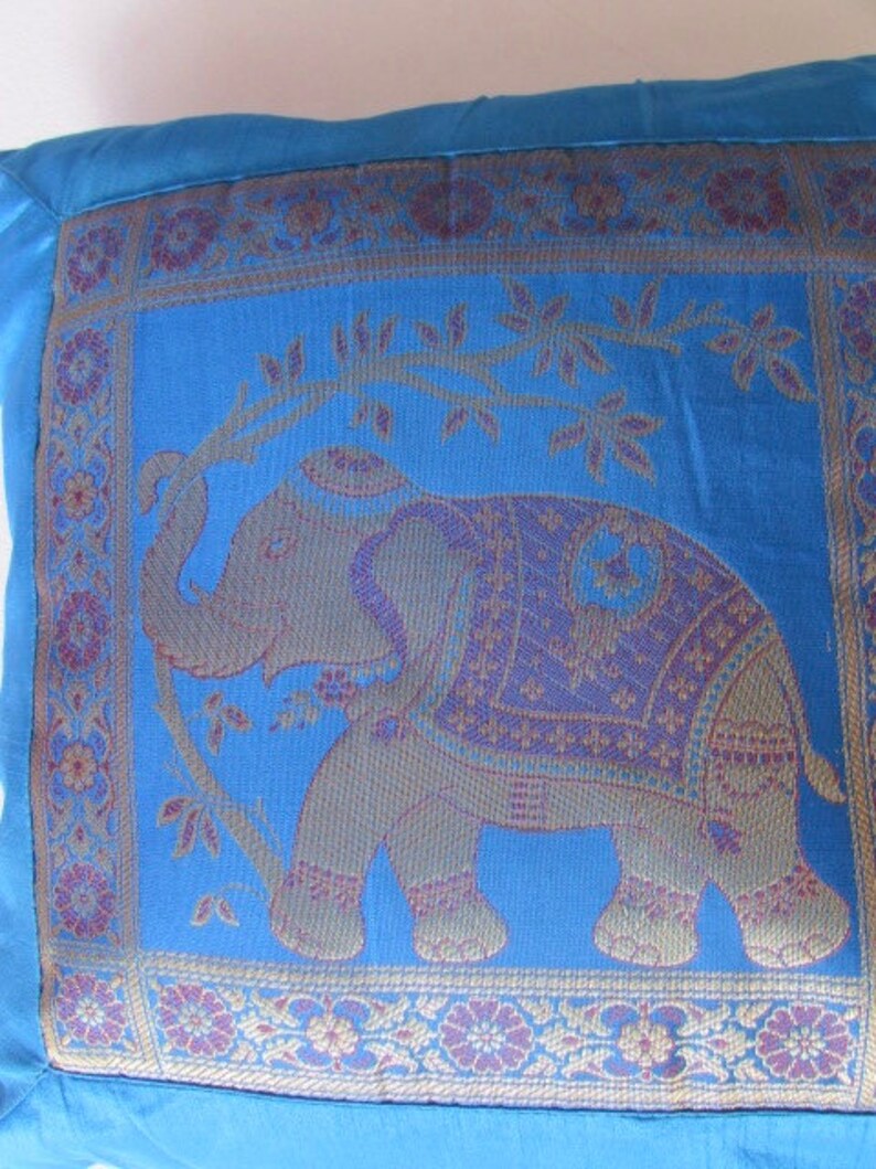 May include: Blue throw pillow with an embroidered elephant design. The elephant is standing on a vine with leaves and flowers. The pillow has a decorative border with floral patterns in shades of purple, gold, and blue.
