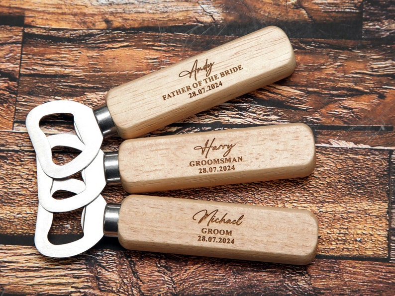 May include: Three wooden bottle openers with engraved names and titles, including "Andy Father of the Bride 28.07.2024", "Harry Groomsman 28.07.2024", and "Michael Groom 28.07.2024".