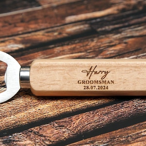 May include: A wooden bottle opener with a metal opener and a personalized inscription that reads "Harry, Groomsman, 28.07.2024".