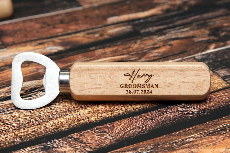 May include: A wooden bottle opener with a metal opener and a personalized inscription that reads "Harry, Groomsman, 28.07.2024".