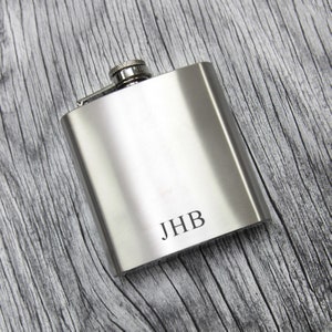 May include: A silver stainless steel hip flask with a screw-on cap and the initials "JHB" engraved on the front.