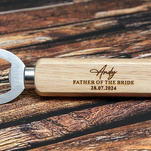 May include: Wooden bottle opener with a metal opener and a personalized inscription that reads "Andy Father of the Bride 28.07.2024".