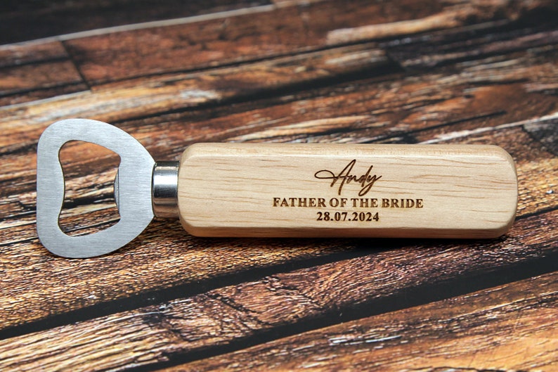 May include: Wooden bottle opener with a metal opener and a personalized inscription that reads "Andy Father of the Bride 28.07.2024".