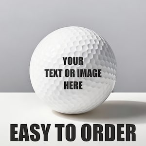 May include: A white golf ball with a dimpled surface. The text "YOUR TEXT OR IMAGE HERE" is printed on the ball. Below the ball, the text "EASY TO ORDER" is displayed in bold, black letters.
