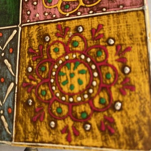 K&ouml;nnte beinhalten: Eine quadratische Fliese mit senfgelbem Hintergrund und einem zentralen magentafarbenen Blumenmotiv. Das Design enth&auml;lt kleine gr&uuml;ne Punkte, wei&szlig;e Akzente und eine strukturierte Oberfl&auml;che. Angrenzende gr&uuml;ne, rosa und blaue Fliesen sind sichtbar.