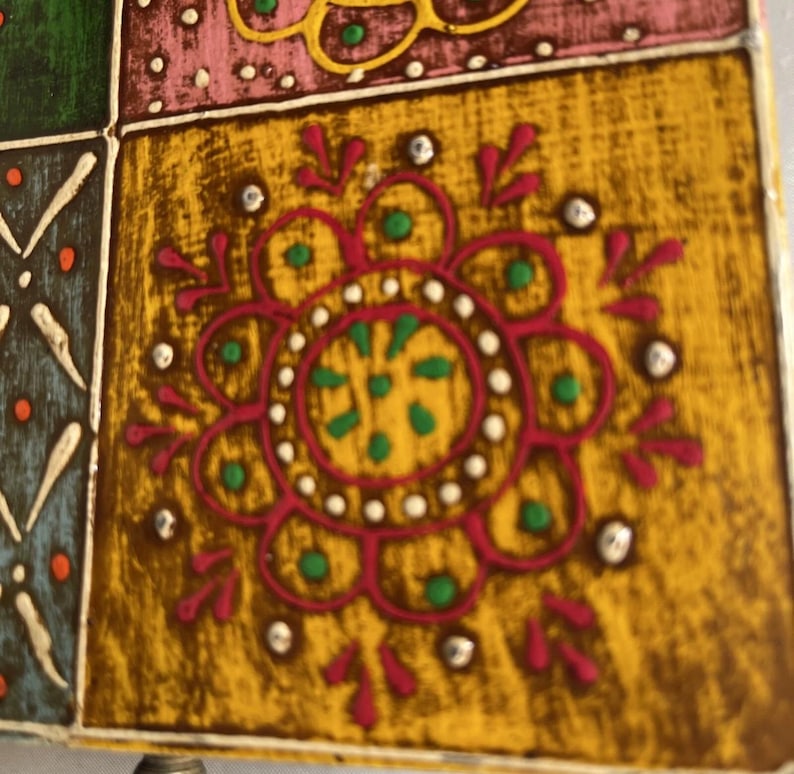 K&ouml;nnte beinhalten: Eine quadratische Fliese mit senfgelbem Hintergrund und einem zentralen magentafarbenen Blumenmotiv. Das Design enth&auml;lt kleine gr&uuml;ne Punkte, wei&szlig;e Akzente und eine strukturierte Oberfl&auml;che. Angrenzende gr&uuml;ne, rosa und blaue Fliesen sind sichtbar.