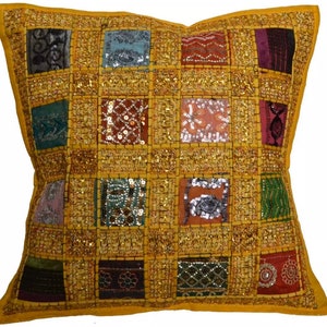 Op de afbeelding: Een vierkant geel kussen met een patchwork ontwerp. Het kussen is versierd met kleurrijke vierkanten van stof, pailletten en borduurwerk.