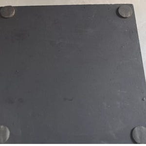 K&ouml;nnte beinhalten: Eine quadratische, mattschwarze Basis mit einer glatten, flachen Oberfl&auml;che. An jeder der vier Ecken auf der Unterseite sind kleine, kreisf&ouml;rmige, dunkelgraue Filz- oder Gummipolster angebracht, die f&uuml;r Stabilit&auml;t sorgen und Kratzer verhindern.
