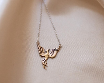 May include: A gold-toned metal necklace featuring a pendant shaped like a stylized bird with outstretched wings and a long tail. The pendant is attached to a delicate, thin metal chain that extends upwards from the wings of the bird figure.