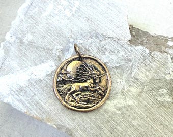 May include: A circular bronze-toned metal pendant featuring a raised relief design of a unicorn galloping across a landscape with a large full moon in the background. The pendant has a small metal loop at the top for attachment to a chain or cord.