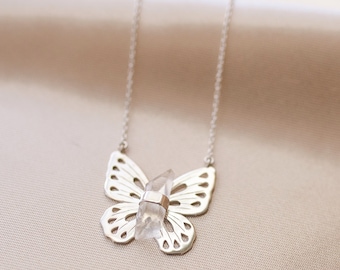 May include: A silver butterfly necklace with a clear quartz crystal pendant. The necklace is delicate and feminine, and the crystal adds a touch of sparkle.