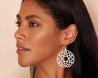 May include: A silver-toned earring featuring a circular, intricate geometric mandala design with a central triangle cutout. The earring hangs from a simple hook wire, showcasing a symmetrical, openwork pattern that radiates outward from the center.