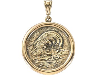 May include: A gold-toned pendant featuring a detailed, embossed image of a wave crashing in the ocean. The pendant is round and has a smooth, polished finish.