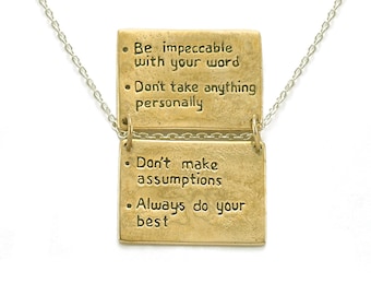 May include: A gold necklace with two rectangular pendants. The pendants have four inspirational quotes engraved on them: "Be impeccable with your word", "Don't take anything personally", "Don't make assumptions", and "Always do your best".