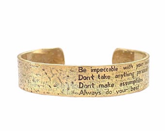 May include: Gold-toned metal bracelet with an inscription that reads: "Be impeccable with your word. Don't take anything personally. Don't make assumptions. Always do your best."