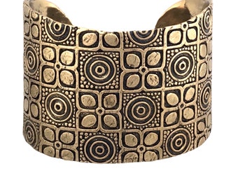 May include: A gold-toned metal cuff bracelet with a geometric pattern of circles and squares.