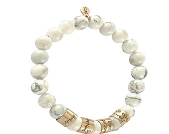 May include: White Howlite beaded bracelet with gold accents. The bracelet features five gold beads with engraved inspirational messages: "Don't  per  some", "D  expectations", "Always", "Be  impacted  word", and "Soar".