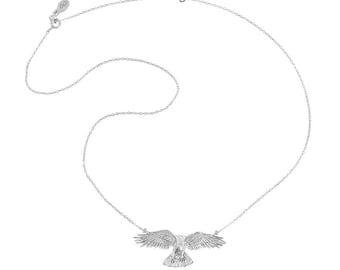 May include: A silver-toned necklace featuring a delicate chain and a central pendant shaped like a bird of prey in flight with wings spread wide. The pendant displays detailed feather textures and is attached to the chain at both wing tips.