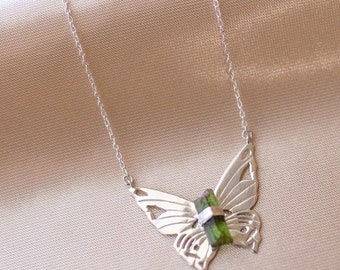 May include: A silver butterfly necklace with a green gemstone pendant. The butterfly is detailed and intricate, with cutouts in the wings.