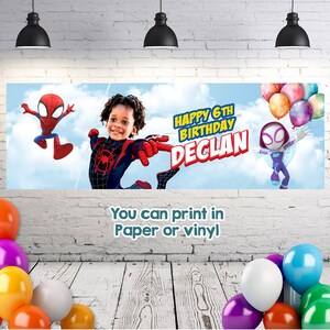 May include: A rectangular birthday banner featuring a blue sky background with clouds, a child in a superhero costume, Spider-Man, and Ghost-Spider. The text reads Happy 6th Birthday Declan. The banner is displayed against a white brick wall.
