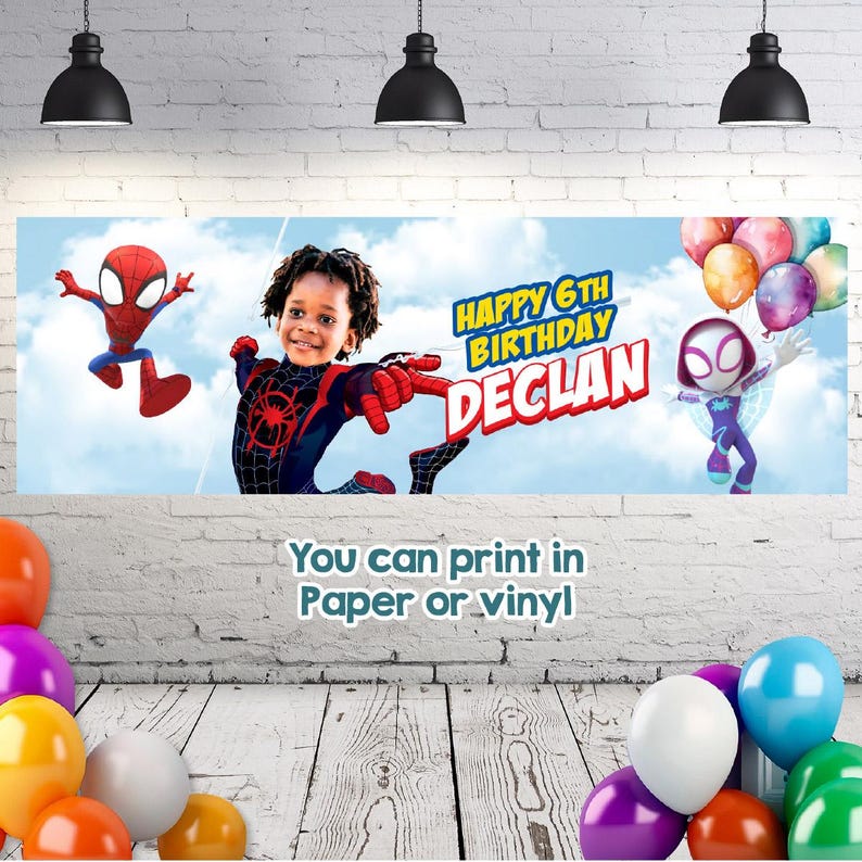 May include: A rectangular birthday banner featuring a blue sky background with clouds, a child in a superhero costume, Spider-Man, and Ghost-Spider. The text reads Happy 6th Birthday Declan. The banner is displayed against a white brick wall.