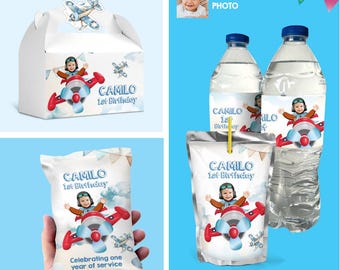 May include: A birthday party favour bundle featuring a blue and white favour box, a blue and white juice pouch, a blue and white water bottle, and a blue and white snack bag. Each item features a cartoon image of a child in a pilot costume flying a red aeroplane. The text "CAMILO 1st Birthday" is printed on each item.