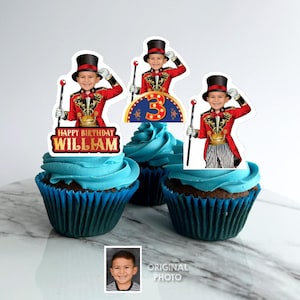 Może przedstawiać: Babeczki z niebieskim lukrem i dekoracjami przedstawiającymi dziecko w kostiumie ringmastera. Jedna dekoracja mówi "Happy Birthday William", druga ma numer "3". Małe zdjęcie dziecka znajduje się w rogu.