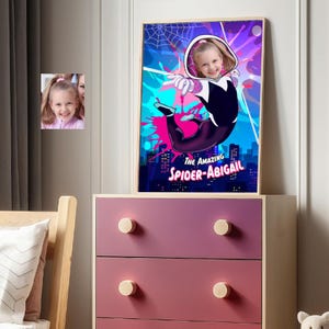 May include: A framed poster featuring a young girl as Spider-Gwen, with the text "THE AMAZING SPIDER-ABIGAIL." The artwork has a vibrant color scheme of pink, blue, and purple. A smaller framed photo of the girl is also visible.