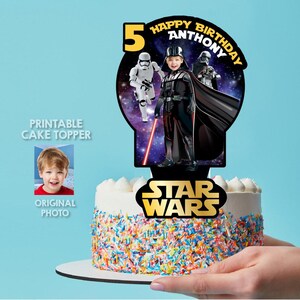 May include: A Star Wars-themed cake topper featuring Darth Vader and a Stormtrooper. The topper is personalized with the name "Anthony" and the number "5". The cake is decorated with colorful sprinkles and white frosting.