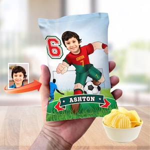 May include: A personalised bag of crisps with a cartoon illustration of a child in a football kit. The design includes the child's image, the name "Ashton", and the number "7". A small bowl of crisps is also visible.