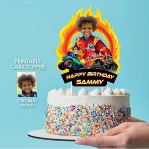 May include: Printable cake topper featuring a monster truck theme with a child's photo in the center. The topper includes a red monster truck, a green monster truck, and flames. The text "Happy Birthday Sammy" is printed on a black banner.