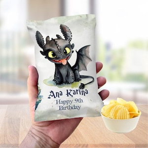 May include: A white chip bag featuring a cartoon dragon illustration with the text "Ana Karina Happy 9th Birthday". The bag is held in a hand, with a bowl of chips in the foreground.