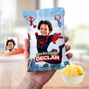 May include: A custom snack bag featuring a graphic of a child dressed as a superhero with a spider emblem on the chest. The bag includes the text Happy 6th Birthday and the name Declan, set against a blue sky and city skyline background.