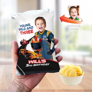 May include: A personalized chip bag featuring a young boy in a racing suit, with the text "Young, Wild and Three" and "Will's 3rd Birthday." The bag includes a photo of the boy and racing car graphics. A bowl of chips is next to the bag.