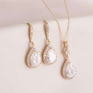 May include: A gold necklace and earrings set with teardrop-shaped clear crystal stones surrounded by smaller stones.