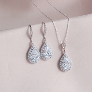May include: A silver necklace and earrings set with pear-shaped cubic zirconia stones. The stones are surrounded by smaller cubic zirconia stones.