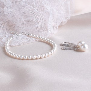 May include: A pearl bracelet and pearl earrings set. The bracelet is made of white pearls and a silver clasp. The earrings are silver with a single white pearl on each earring.