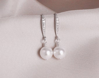 May include: A pair of silver dangle earrings with a pearl drop and a row of clear cubic zirconia stones.