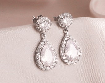 May include: A pair of silver teardrop earrings with a large clear crystal surrounded by smaller crystals.