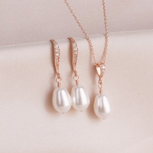 May include: A set of rose gold jewelry featuring a delicate necklace and matching earrings. The necklace and earrings have a small row of clear cubic zirconia stones and a single pearl drop.