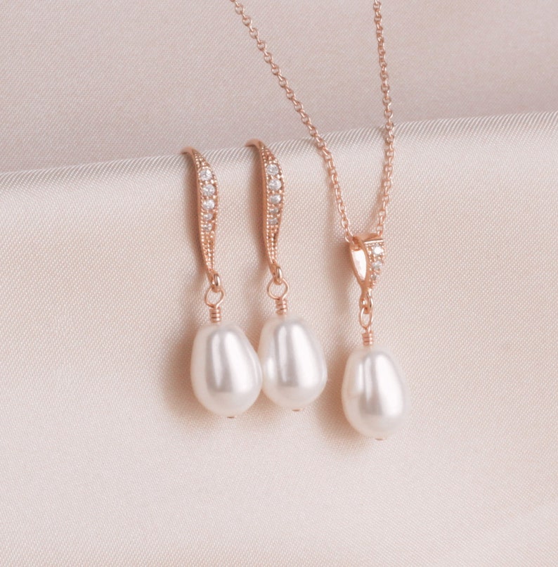 May include: A set of rose gold jewelry featuring a delicate necklace and matching earrings. The necklace and earrings have a small row of clear cubic zirconia stones and a single pearl drop.